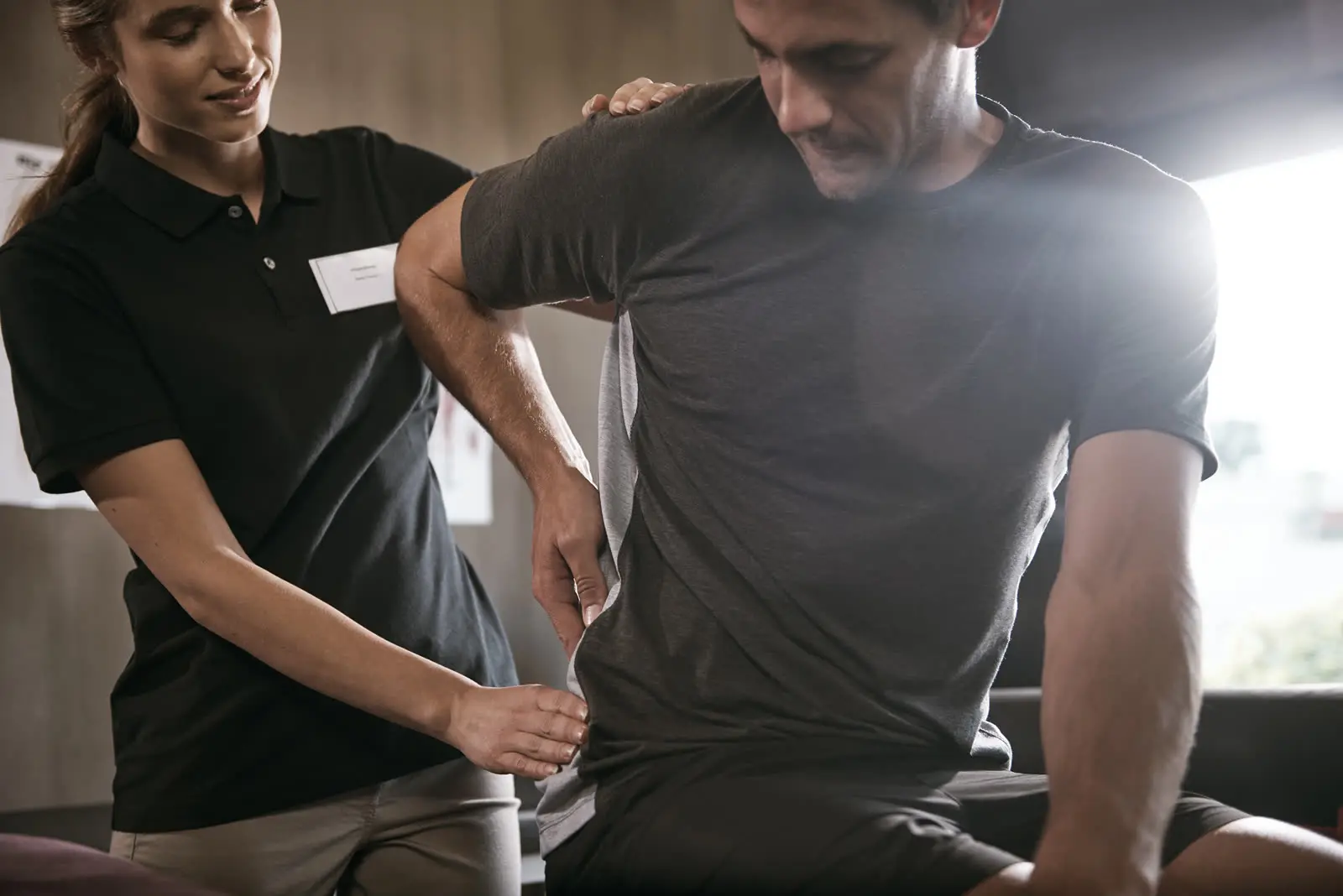 Physiotherapeutin behandelt einen sitzenden Patienten am Rücken