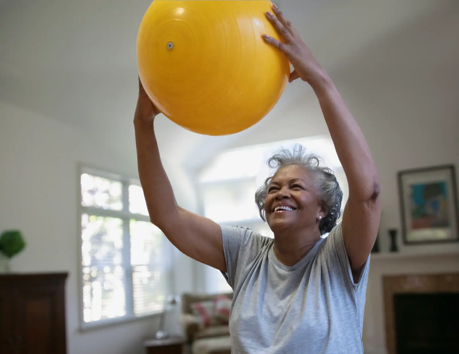 Seniorin übt mit einem Gymnastikball in ihrem Wohnzimmer